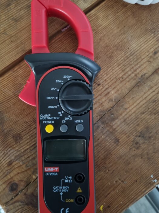 Multimeter av märket UNI-T UT200A med röd och svart design, placerad på ett trämönstrat bord.