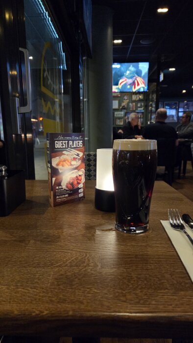 Ett glas mörkt öl på bordet, ett stearinljus och en meny i en restaurang.