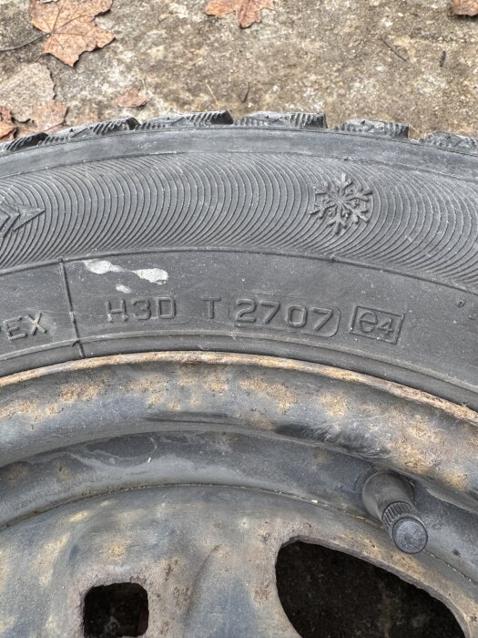 Bilden visar ett däck med märkningen "2707" och en snöflinga, vilket kan indikera tillverkningsdatum och vinterdäck.