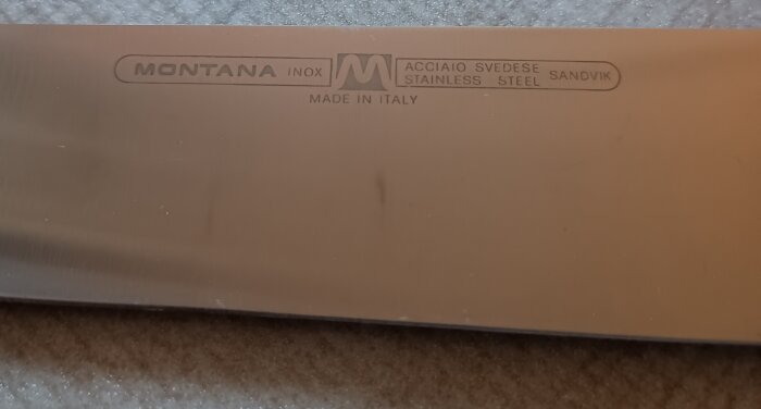 Närbild av en kniv med texten "Montana" och "Made in Italy" samt "acciaio svedese stainless steel Sandvik" på bladet.
