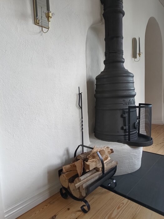 Vedkorg med vedträn bredvid en Järlekamin på ett trägolv.