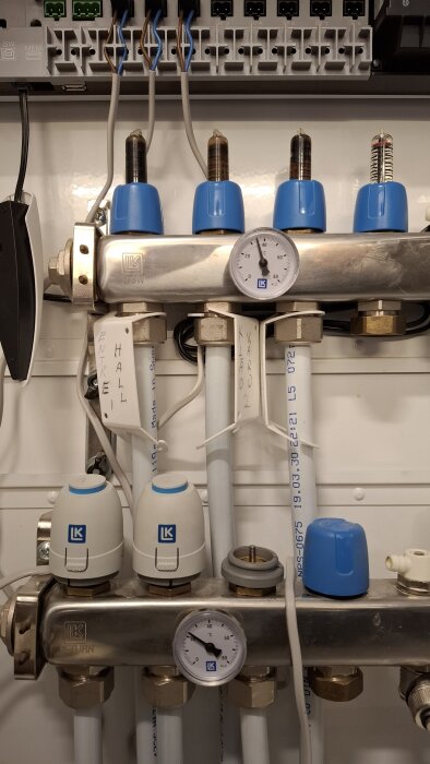 Golvvärmesystem med tre slingor, två anslutna med ventiler och en termostat. Termodon borttaget från en slinga, ventiler synliga, samt tryckmätare.