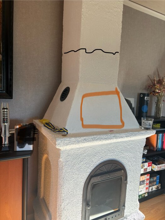 Inbyggd kamin från 1990 med synlig spricka och ventilationsöppning, omgiven av märken i svart och orange för möjliga förändringar.