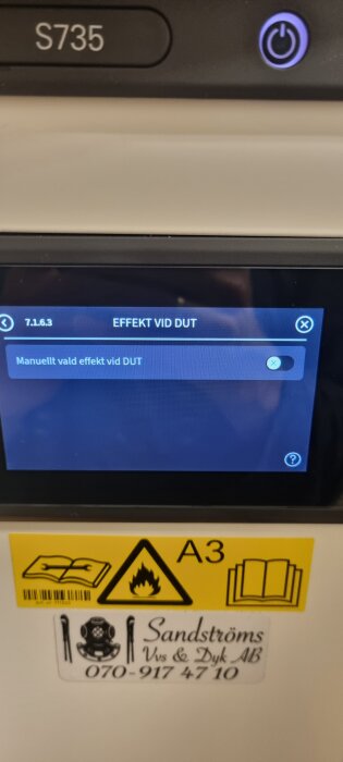 Närbild av värmepumpens display som visar inställningen "Manuellt vald effekt vid DUT", med varningssymbol och företagsklistermärke nedanför.