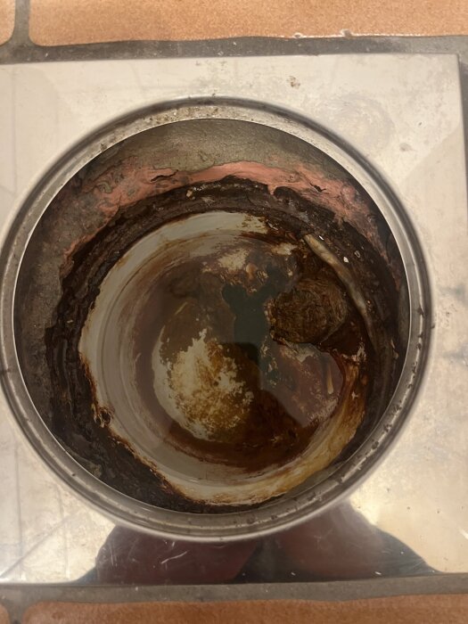 Rostig golvbrunn i källare av gjutjärn och plast, med tydliga rostskador.