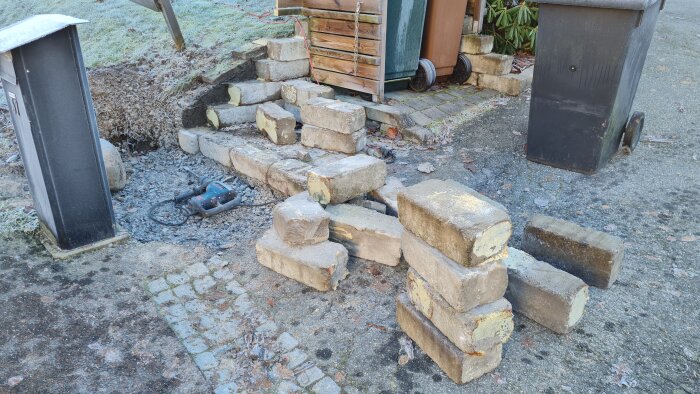 Bitar av en rivningsmur med staplade stenar omgivna av grus. En borrhammare ligger på marken bredvid.