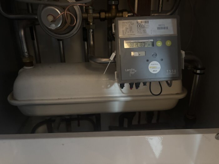 Expansionskärl i en uppvärmningsanläggning med anslutna rör och en mätare av märket Landis+Gyr.