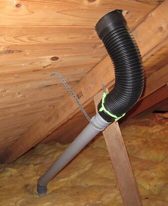 Avloppsluftning med ett svart korrugerat rör och en grå koppling i ett kallt utrymme, fastsatt mot takbjälkar.