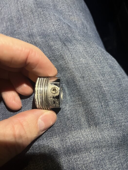 Användare håller i en metalladapter utan packning, mot en blå jeansbakgrund.