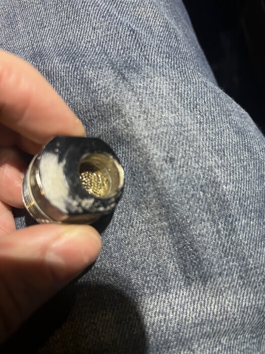 Hand håller en metalladapter utan packning på jeansklädd bakgrund, relaterat till en diskussion om installation.