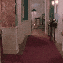 En person springer längs en röd matta i en upplyst hall i ett hem.