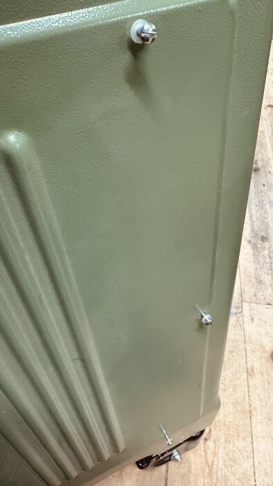 Grön sidoplåt av en Ulmia tallriksslip med monterade skruvar och plastbrickor mot ett trägolv.