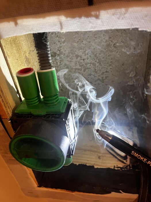 Täthetsprovning av källarvägg med rökpenna och gröna ventilationskomponenter synliga i träram.