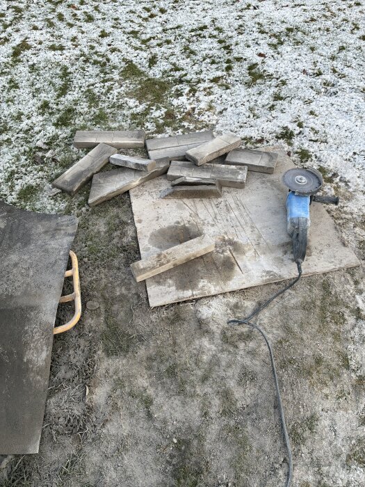 Bitar av kapade stenar ligger på marken bredvid en vinkelslip, omgivna av frostigt gräs.