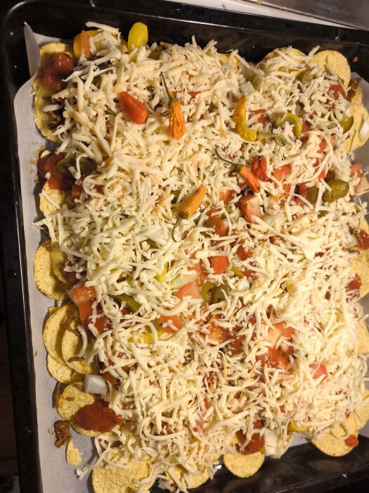 Nacho gratäng med ost, skivade chili, tomater och salsa på en bakplåt, förberedd för gräddning i ugn.