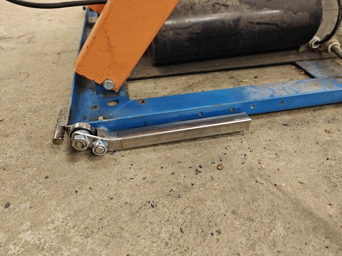 Golvmontering med ett blått fyrkantsrör, orange vinkel, kullager och muttrar; del av byggprojekt för justerbart bord.