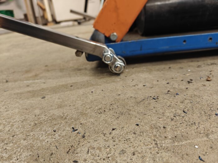 Närbild av hemmagjord anordning med kullager och fäste i fyrkantsrör på verkstadsgolv.