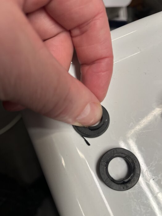 En hand håller en svart tätning som placeras på en vit yta, med en annan tätning bredvid. Diskussionen handlar om läckage och väggskador.