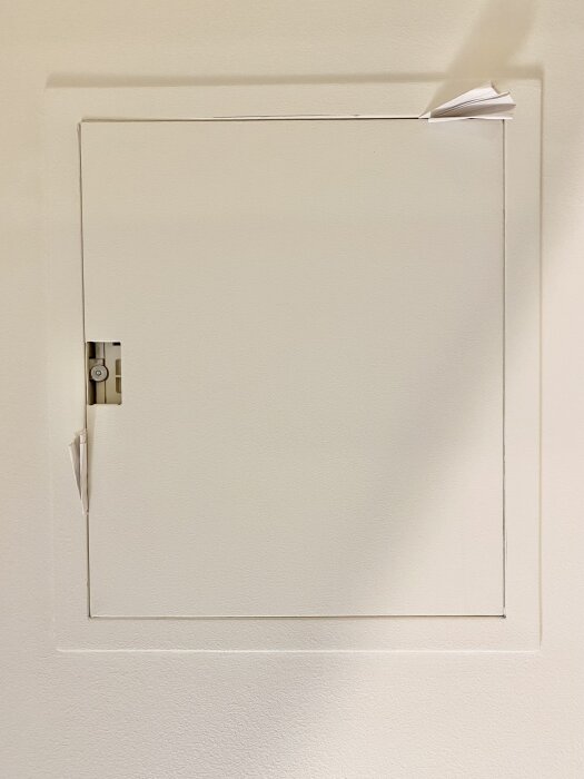 Inbyggt säkringsskåp utan gångjärn och lås, dörren fastkilad med vikta pappersbitar.