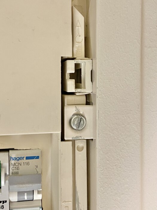 Inbyggt säkringsskåp med synlig trasig hänganordning, skruv och del av elcentral, gulaktig plastram med slitna kanter.