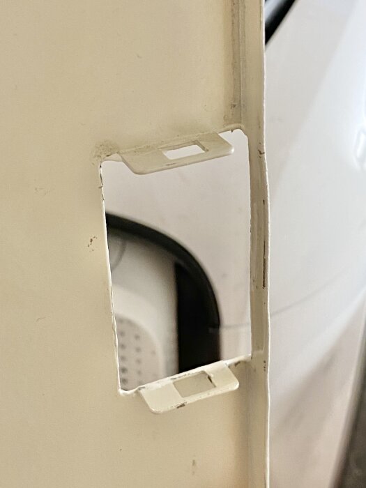 Närbild på hörn av ett inbyggt säkringsskåp utan gångjärn, med vitt avskavt material och en öppning där luckan ska fästas.