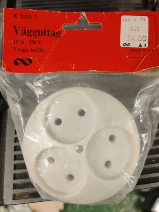 Förpackat ojordat vägguttag med tre hål för anslutning, etikett visar priset 14kr.
