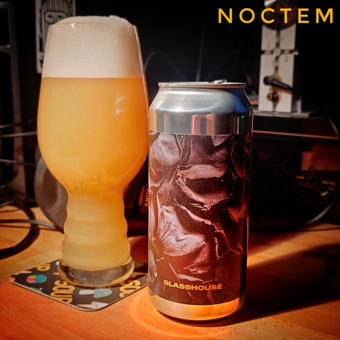 Ölglas fyllt med skummig öl bredvid en konserverad dryck med etiketten "Glasshouse" på ett bord.