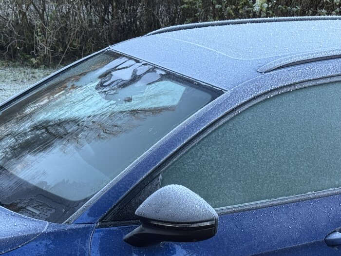 Bil med frostig vindruta en kall morgon, där övre delen av rutan har värmts och is har smält, visar effektiviteten hos elektrisk vindruteuppvärmning.