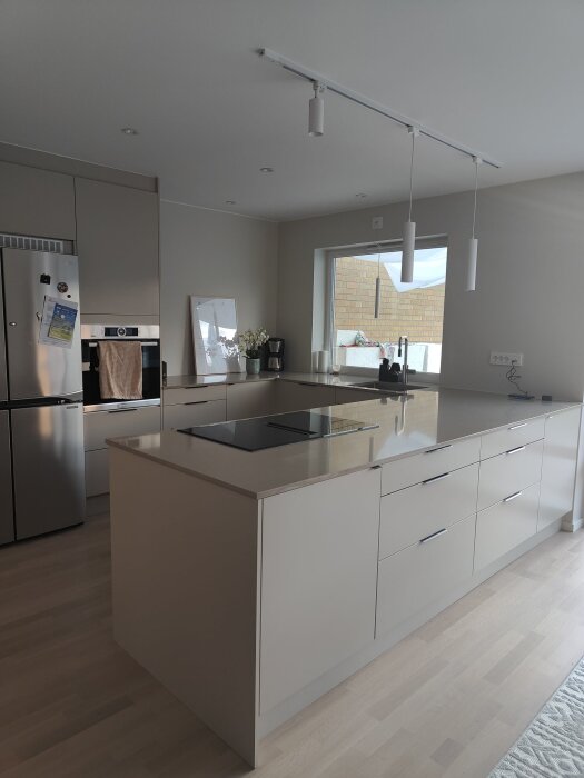 Modernt U-format kök med integrerad spishäll och ugn, vita skåp, och stilsäkra hängande lampor, nära placerat köksfönster.