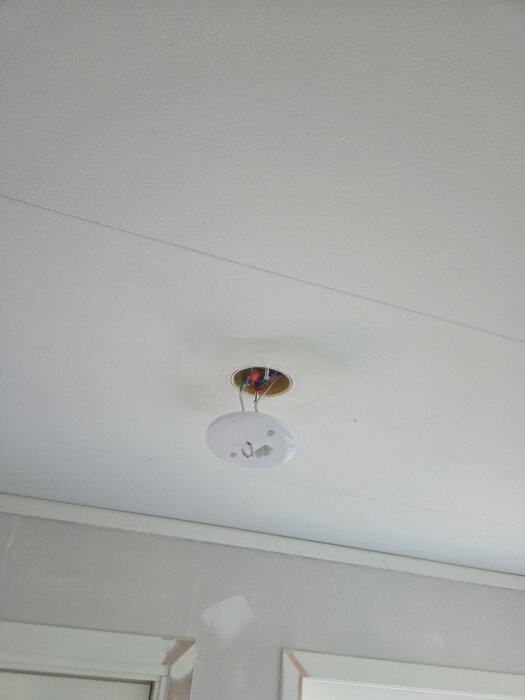 Nytt DCL-lamputtag är installerat i ett vitt innertak, med synliga elledningar ovanför och en pågående renovering av bostaden synlig i bakgrunden.