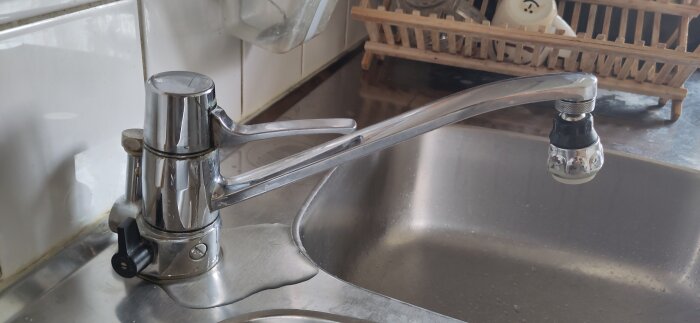 Äldre köksblandare i metall utan tillverkarlogga, troligen från 90-talet, monterad över en diskho med vattenläckage.