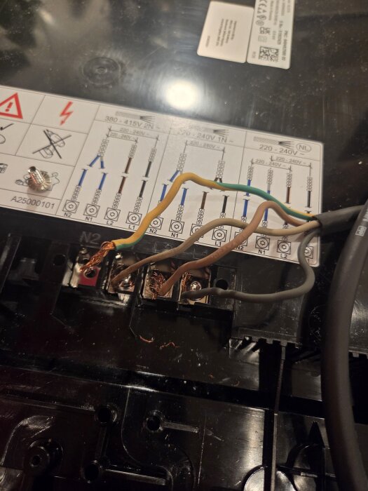 Kablar anslutna till kopplingsplint med etiketter inklusive N2, reflektion av en lampa ovanpå ytan.