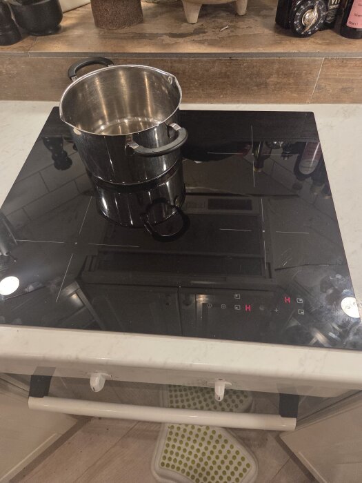 En kastrull på en svart induktionshäll som är påsatt, med två röda "H" på hällens display.