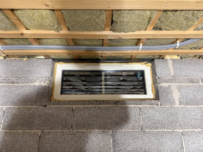 Källarfönster med synlig isolering och träreglar i taket, syllen av stål ses över fönstret; visar konstruktion och möjlig köldbrygga.