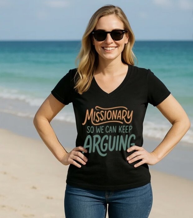Kvinna i solglasögon står på en sandstrand, klädd i en svart T-shirt med texten "Missionary So We Can Keep Arguing".