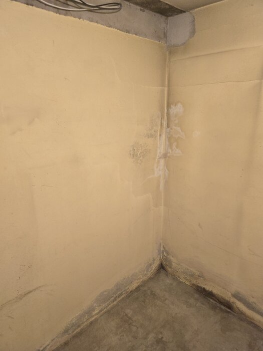 Gul källarvägg med gamla sprickor och fläckar som ska slipas och målas. Golvet är av betong, och elinstallationer planeras för rummet.