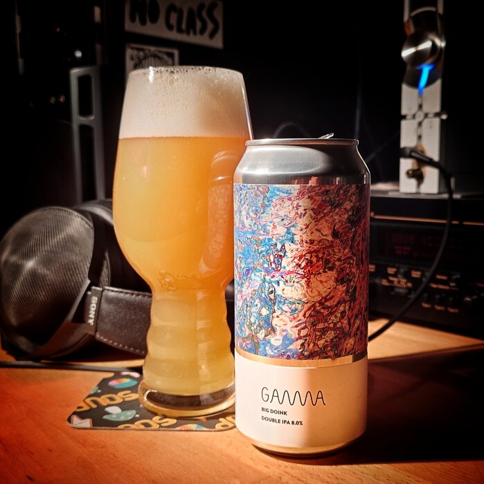 En ölburk med etiketten "Gamma Big Doink Double IPA 8.0%" bredvid ett glas med skummande öl på ett bord.