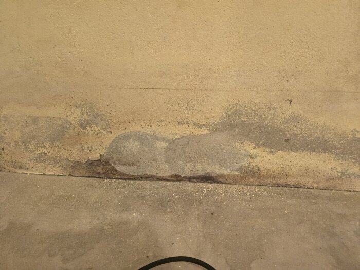 Slipningsarbete på murad vägg; gul färg har delvis slipats bort, avslöjande exponerad yta och damm på golvet.