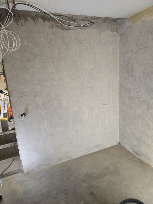 Slipad vägg och golv i källare, med kablar i taket och en elektrisk uttagsinstallation synligt. Väggstruktur syns tydligt efter slipning.