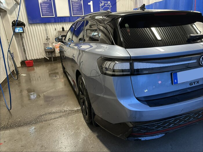 Grå bil av modellen ID7 GTX i en biltvätt på OKQ8, synlig bakifrån med blöta spår på golvet och en röd hink i bakgrunden.