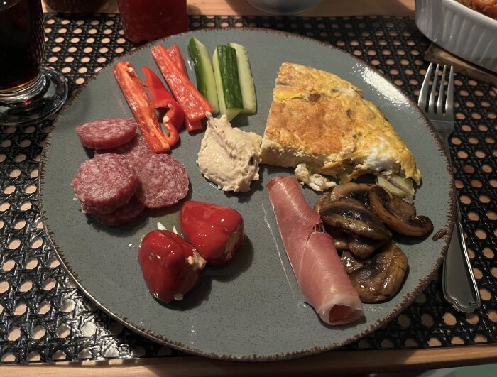 Tallrik med tapas: salamiskivor, paprika, gurka, omelett, prosciutto, svamp och fyllda paprikor.