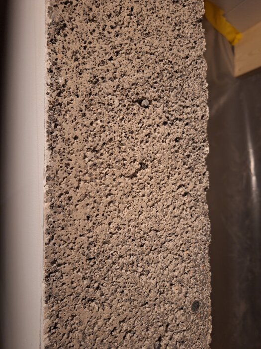 Grovt texturerad vägg som ser ut att vara av lättbetong, med en liten utskjutande skruv i mitten av bilden.