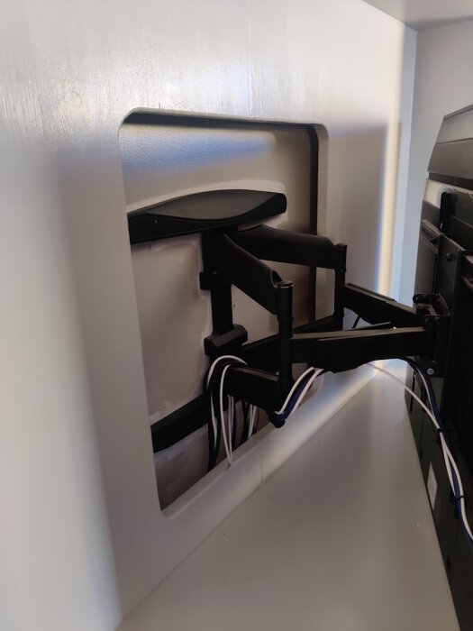 TV-inställningar bakom panel med kablar dolda av furu limfog, visar monteringsarm och kabelhantering.