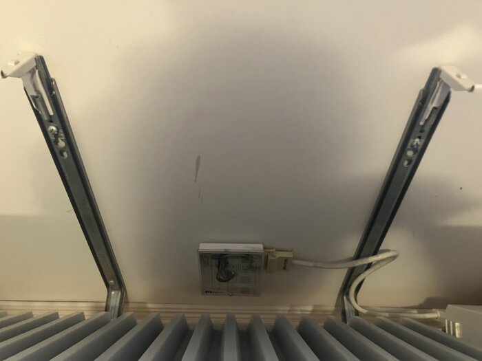 Väggmonterad elementhållare utan termostat, med eluttag och kabelanslutning i mitten.