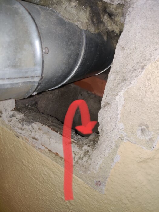 Metallventilationsrör i en vägg med synlig kanal under ventilhål, markerad med en röd pil.