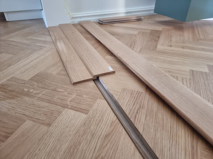 Tröskelplattor i trä på ett golv med fiskbensmönster, förbereds för installation över en övergång med nivåskillnad.