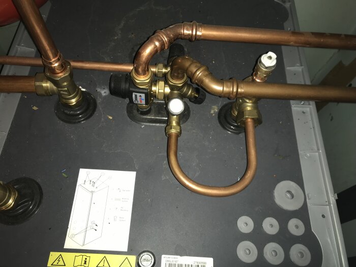 Kopparrör, ventiler och reglage i ett tekniskt system, uppmonterade bredvid en förteckning med beskrivningar.