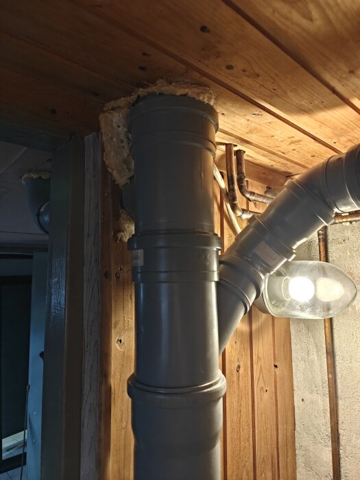 Grå avloppsrör genom ett bastutak med PU-skum runt rören i ett 50-talshus.