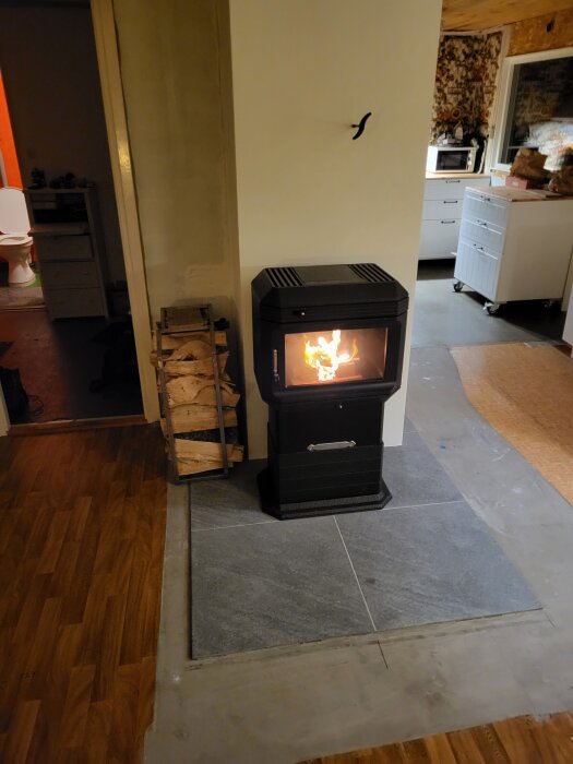 Braskamin installerad vid nymålad skorsten, placerad på stengolv, med vedförvaring intill.