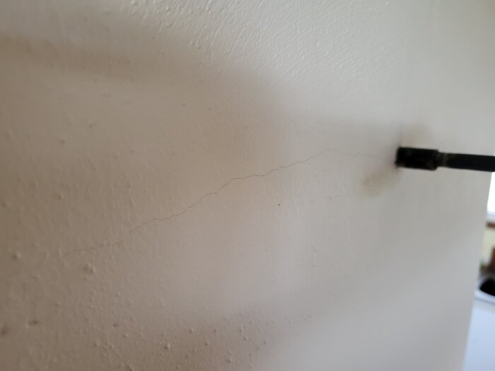 Spricka i vitmålad murad vägg nära kaminens spjällreglage.